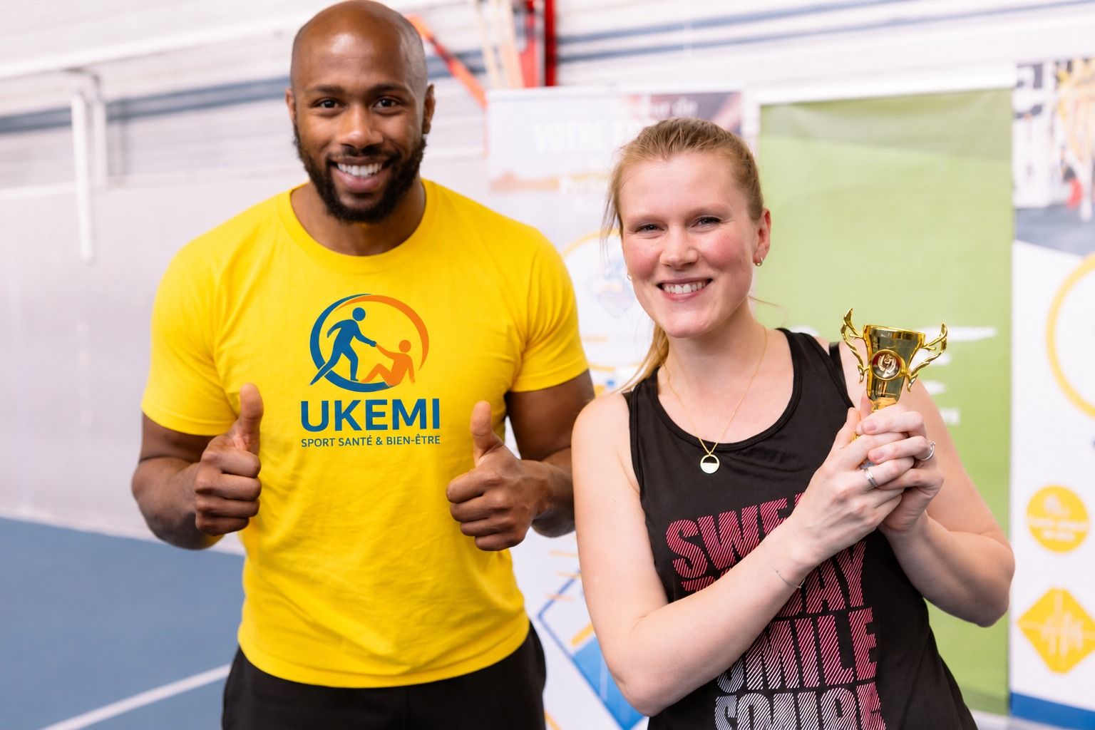 Un intervenant UKEMI, en t-shirt UKEMI, aux côtés d'une participante qui tient un trophée.